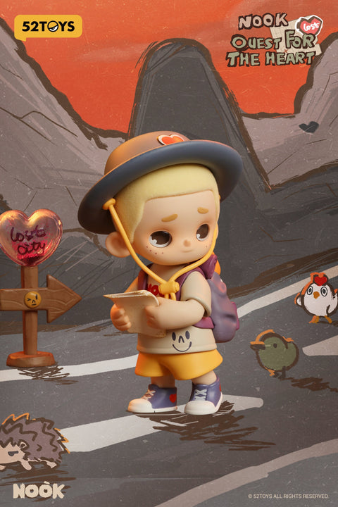 From the 52TOYS Nook “Quest for the Heart” blind box series, this figure shows a blond boy wearing a wide-brimmed hat, yellow shorts, and a backpack, standing on a road while reading a map. A heart-shaped sign labeled “Love City” points in one direction, while small animal companions—a hedgehog, bird, and chicken—appear around him, set against a mountainous orange-hued background.