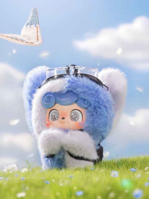 A blue Qkid plush with fluffy ears and goggles looks up as a paper airplane flies overhead. The plush has soft blue curls, silver-gray eyes, and a curious expression. It stands on a grassy hill under a bright sky with white clouds and scattered flower petals.