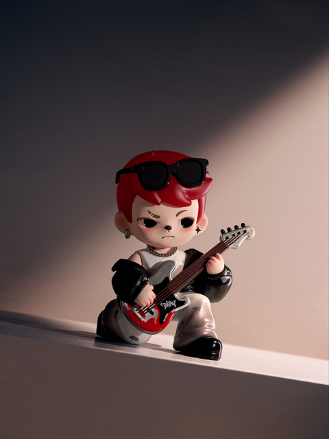 A red-haired figure wearing black sunglasses and metallic pants kneels under a spotlight, holding a red electric guitar with “Rayan” written on it. The character’s pose and expression convey cool determination against a dark stage backdrop.