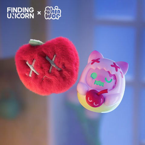 Two small figures float against a softly lit background. On the left is a plush red heart-shaped toy with embroidered gray X eyes and a small green stem on top. On the right is a smooth lavender vinyl cat figure with mint-green eyes, wearing a hood with red X marks and holding a red cherry with a smiling face.