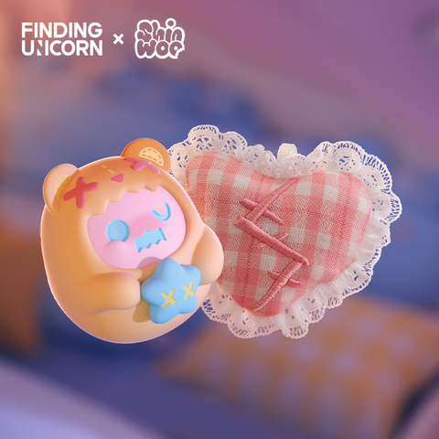 A small orange vinyl bear figure with a pink face and X marks on its hood floats beside a red-and-white checkered heart plush. The plush has lace edges and stitched red X marks. The figure holds a light blue star pillow and appears under soft bedroom lighting