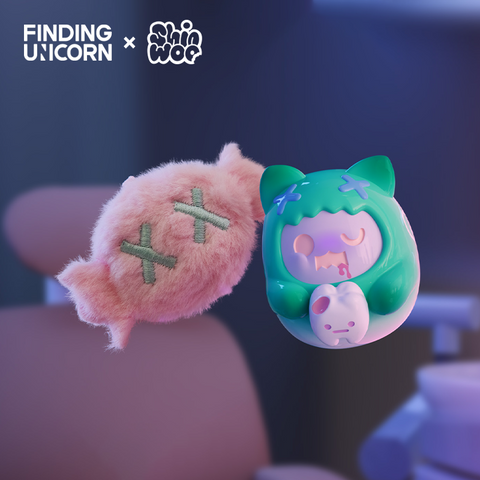 A small pink candy-shaped plush with two stitched green X marks floats beside a mint green vinyl cat figure. The vinyl character has rounded ears, matching green X marks on its hood, and holds a white candy with a small pink face. The scene is softly lit in cool purple tones.