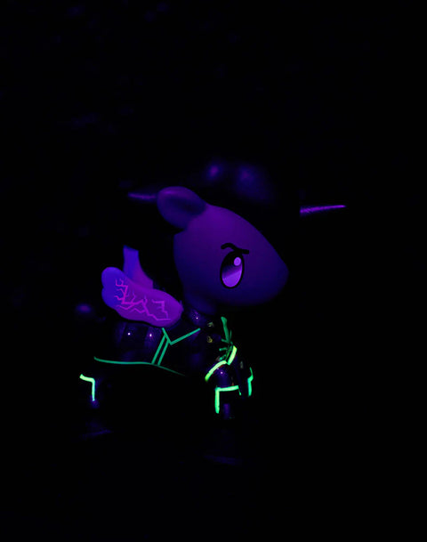 The Silco Unicorno glows under blacklight, showing neon green circuitry-like accents across the legs and torso. The black mane and red horn appear darker, while the purple wings and face catch subtle violet highlights. The chrome sections recede into shadow, emphasizing the glowing linework.