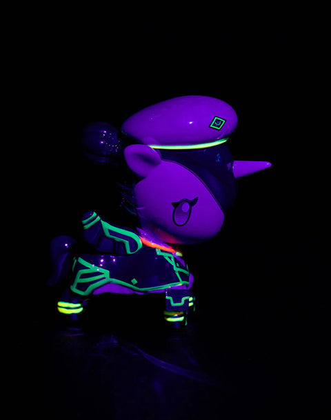 Under blacklight, the Caitlyn Unicorno displays glowing neon green outlines across her uniform and legs. Her officer hat takes on a smooth purple cast, while the horn glows a striking bright yellow. The figure’s hair and wings appear saturated with deep purples illuminated by fluorescent highlights.