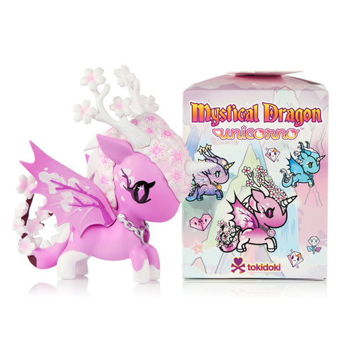 This image shows the Tokidoki Unicorno Mystical Dragon Cherry Blossom figure next to the official Mystical Dragon blind box. The pink dragon-unicorn has blossom details, translucent wings, and a silver chain. The illustrated box behind it displays artwork of multiple dragon designs.