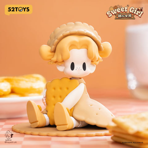 A biscuit-themed figurine girl with blonde hair, freckles, and a lacy bonnet. She hugs a scalloped rectangular soda cracker, seated on a matching cracker base with a warm, homely look.
