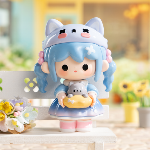A chibi-style figure with long blue pigtails wears a pale lavender wolf hood with cross eyes, a blue dress, and pink shoes. She holds a small gray wolf pup sitting in a yellow dish. The background is soft and dreamy with flowers, giving the toy a playful yet gentle fairy-tale aura.
