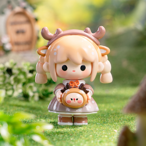 A light brown-haired girl with tiny antlers wears a brown dress with white polka dots and a small orange bow. She holds a round companion shaped like a reindeer with antlers. Set against a forest backdrop, the figure radiates cozy woodland holiday charm and soft festive fantasy detail.