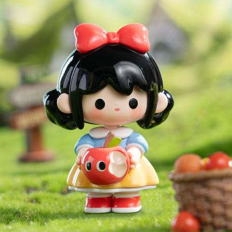 A Snow White-inspired figurine with short black hair and a red bow. She wears a classic yellow and blue dress and holds a red apple plush with a tiny face. Set in a grassy backdrop with baskets of apples, the design reflects the iconic fairy tale with a cute twist.