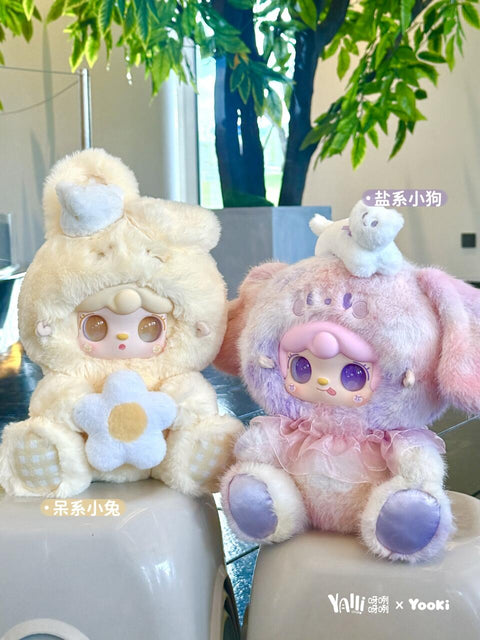 Two plush figures are displayed against a green plant backdrop. The cream bunny holds a white and yellow flower with gingham paws, while the lilac-pink puppy wears a tulle skirt and has a small white animal perched on its head. Both show delicate embroidered details.