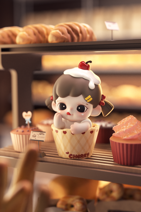 A cute figurine of a girl peeks out from a yellow checkered cupcake wrapper labeled “Cherry.” She has brown hair tied with red ribbons, whipped cream and a cherry on top of her head, and red heart prints on the cup. She’s surrounded by pastries and cupcakes in a bakery display.