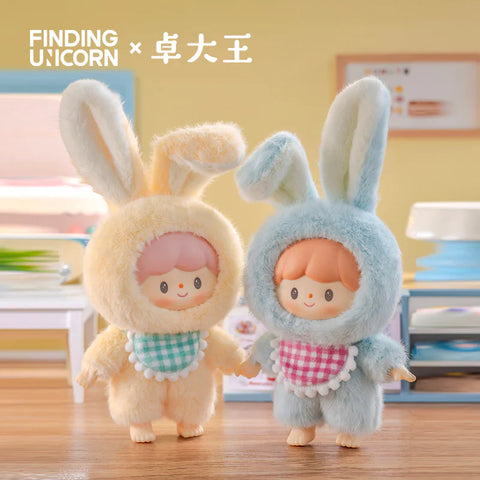 Two plush figures from the Finding Unicorn × 卓大王 Zoton Delicious Bunny Plush Series Blind Box are featured in a cozy, pastel-toned indoor setting. On the left, "Cheese Bunny Zoton" wears a soft yellow bunny suit with upright ears and a green gingham bib. On the right, "Sea Salt Bunny Zoton" is dressed in a light blue bunny outfit with matching ears and a pink gingham bib. Both have cheerful expressions and pastel-colored hair, evoking a warm, playful atmosphere.