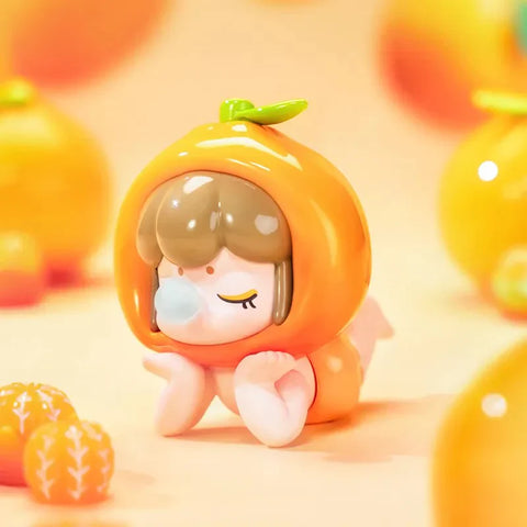 This image showcases a charming collectible figurine from the Baby Nanci Fruits Series Blind Box collection. The figure has a peaceful expression with closed eyes and rests its hands gently on its cheeks. It wears a glossy, vibrant orange-themed headpiece, resembling a fresh mandarin with a small green leaf on top. The character’s short brown hair complements the warm tones of the fruit design. The soft, pastel orange background is adorned with miniature, translucent orange decorations.