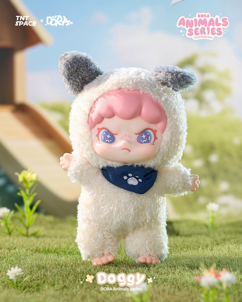 This plush doll wears a fuzzy white dog suit with gray floppy ears and a navy pawprint bandana. Its pink hair and shimmering indigo eyes stand out against the fluffy costume. The barefoot figure stands on lush grass dotted with tiny white flowers, suggesting a calm countryside setting.