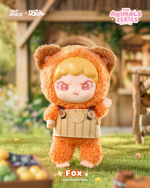 A plush figure in a bright orange fox suit with textured fur, pointy ears, and brown accents. It wears beige corduroy overalls with large buttons and a pocket, giving it a woodland look. The doll has pale skin, strawberry-blonde hair, and glittery red eyes while standing in a rustic outdoor village setting.