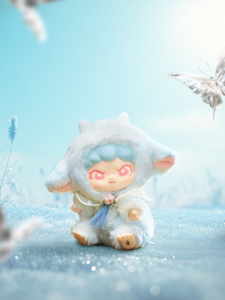 Seated baby‑lamb plush in pale blue fur with tiny white horns and a sky‑blue tassel charm rests in sparkly frost. Butterflies blur at the edges while a bright, cloudless sky adds crisp light to the character’s coral eyes and soft woolly details.