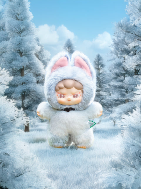 Small plush figure in a frosty blue bunny hood with tall pink‑lined ears stands in a winter forest. Snow‑dusted conifers frame the scene under a bright blue sky, while the toy’s determined gaze and fluffy suit suggest an icy, adventurous spirit.