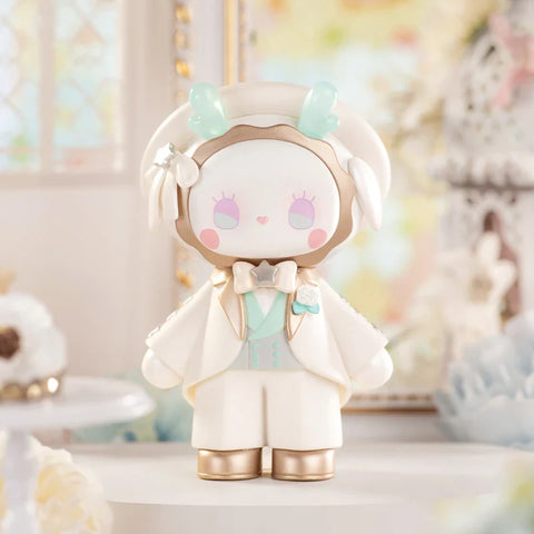 A refined figurine from the "Emma Secret Forest: Beloved Series" stands elegantly in a dreamy, pastel wedding setting. The character wears an ivory tuxedo with gold accents, a mint-green vest, and a star-shaped bowtie. A wide-brimmed hat adorned with flowers and translucent blue antlers adds a magical touch. Soft pink heart-shaped details enhance its charming expression. The delicate background, featuring lace, flowers, and vintage décor, creates a romantic, fairytale-like atmosphere.