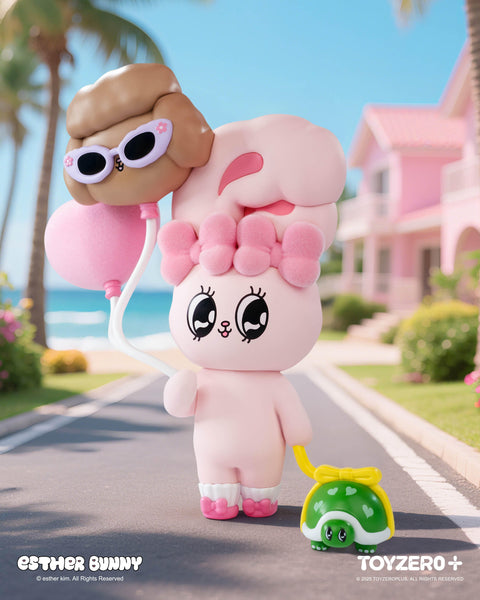 A pastel pink Esther Bunny figurine with a fluffy bow and big sparkling eyes strolls down a sunny seaside street. It holds two balloons, one shaped like a face wearing sunglasses, while pulling a cute green turtle toy with a yellow bow. A pink beach house and palm trees frame the background.