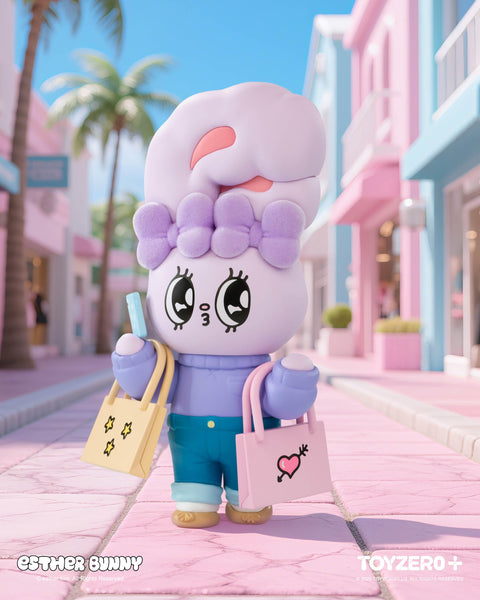 A lavender Esther Bunny figurine with a fluffy purple bow and wide sparkling eyes strolls down a pastel street. Wearing jeans and a lilac sweater, it carries two shopping bags, one yellow with stars and one pink with a heart design, while holding a popsicle under sunny palm trees.