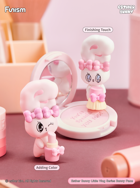 Makeup-themed bunnies, one holding a lipstick tube with a wink, and another standing on a compact mirror in a skirt accessory, as if applying blush. The soft pink vanity setting highlights beauty, charm, and transformation.