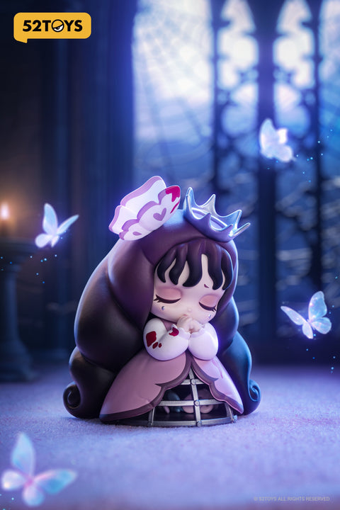Close-up of the “Butterfly Cage” figure from 52TOYS’ Lilith: The Century of Mary series. The character kneels with eyes closed and hands clasped in prayer, wearing a purple and pink gown with a visible cage structure at the hem. Her long hair flows behind her, topped with a metallic crown and a heart-accented flower. Surrounded by glowing butterflies and soft lighting, she appears enclosed in a cathedral-like space with gothic windows and a cobweb in the background, evoking a mood of gentle sorrow and hope.