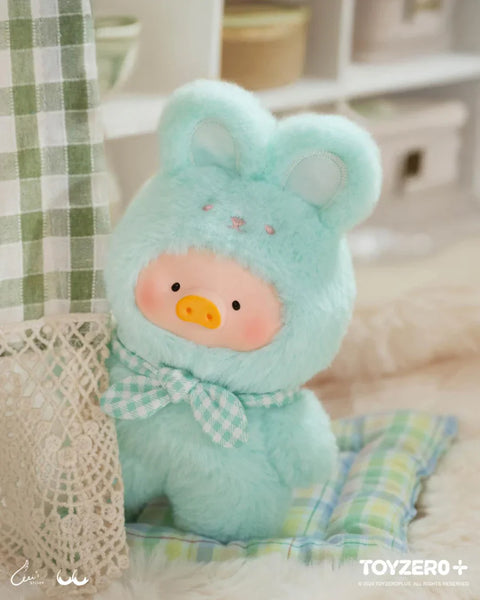 A charming plush from the "LuLu The Piggy: Joyful Time Series" features LuLu dressed in a soft, mint-green bunny costume with embroidered details and floppy ears. It wears a matching gingham bow, adding to its playful look. With rosy cheeks and an innocent expression, the plush peeks out from behind a lace curtain, creating a cozy and whimsical scene. A pastel plaid cushion and warm-toned decor enhance the plush’s adorable and comforting appeal.