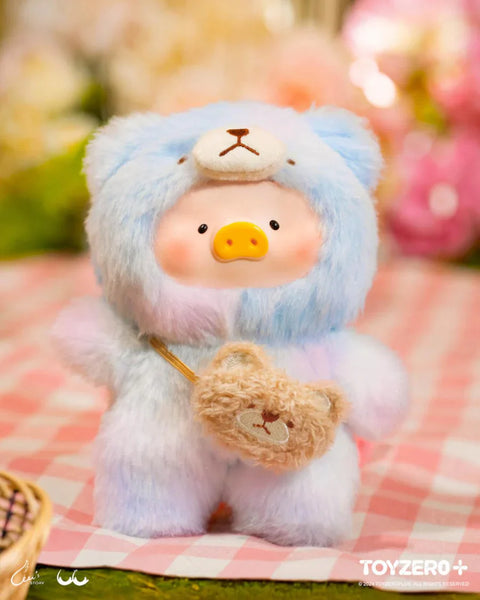 A delightful plush from the "LuLu The Piggy: Joyful Time Series" features LuLu dressed in a soft pastel blue teddy bear costume with an embroidered bear face on the hood. It carries a tiny plush bear bag, adding extra charm. With rosy cheeks and a gentle expression, the plush sits on a pink gingham picnic blanket, surrounded by blurred floral decorations and warm lighting, creating a cozy, cheerful atmosphere perfect for this adorable collectible.