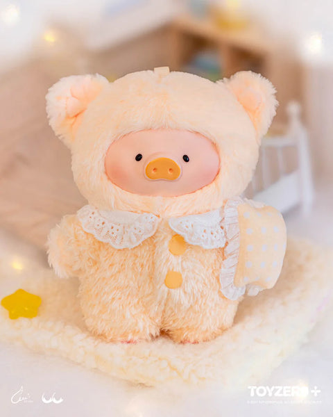 A plush pig wearing a cream-colored fuzzy suit stands on a soft blanket. The suit includes rounded bear ears, a lace collar, and yellow buttons. A small matching pillow with polka dots and ruffled edges is tucked under one arm. The clean setting and symmetrical details highlight a disciplined bedtime theme.