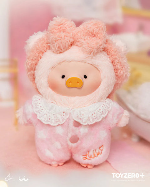 A plush pig in a pink fuzzy suit with fluffy ears stands against a glowing pastel backdrop. The suit has white star patterns, a lace collar, and embroidered text. The pig’s gentle round expression and soft lighting enhance its radiant hidden-chaser identity within the Dreaming Wonderland theme.