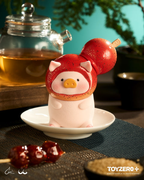 A LuLu the Piggy figure wearing a glossy, red-glittered tanghulu headpiece. The figure stands on a saucer next to a glass teapot and a traditional skewer of candied fruit.