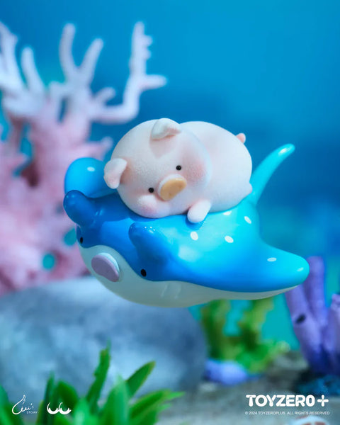 A LuLu the Piggy figure from the Ocean Series by 52TOYS and ToyZero+ is peacefully lying on top of a smiling blue stingray with white spots. The pig has a soft, flocked texture and a calm expression, evoking a dreamy underwater ride. Surrounded by coral, sea plants, and soft lighting, the scene captures a gentle and serene moment in a whimsical ocean setting.