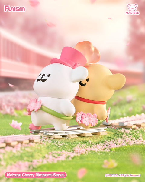 Two Maltese bears ride a cherry blossom–themed rail cart, one white with a pink top hat and one tan with a red collar. They glide past a scenic spring landscape full of drifting pink petals.