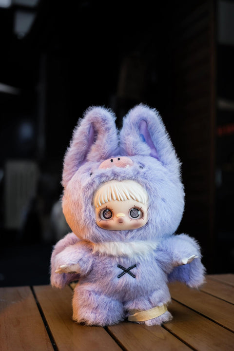 Light purple plush bat doll with large ears, small white fangs, and wings. It has grey spiral-patterned eyes and a black "X" stitched on its chest.