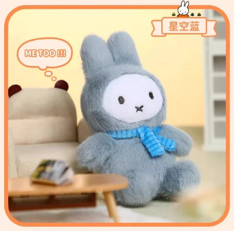 A soft plush bunny figure dressed in a muted blue macaron-inspired outfit with long upright ears and a rounded body. The plush has a white face with small black eyes, an X-shaped mouth, and a knitted blue scarf tied around the neck, giving a calm, cozy appearance.
