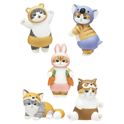 Five cat figurines dressed in playful animal costumes are arranged among pastel household items. One stands on a yellow bottle, another sits on a pink container, while others pose near makeup brushes and an eyeshadow palette. Each costume differs, including bear, dog, bunny, koala, and fox themes, creating a colorful decorative scene.