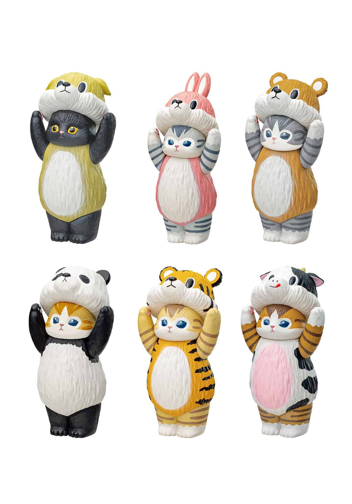 Six cat figurines dressed in soft vinyl animal costumes stand arranged on a light-colored tabletop near decorative props. Each figure holds an animal hood above its head, including dog, bunny, bear, panda, tiger, and cow designs. A small platform and soft floral accents frame the brightly lit display.
