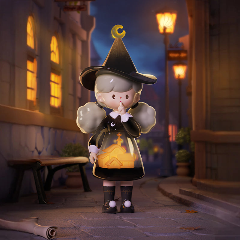 A vinyl figure stands in a lamplit street at night, wearing a black witch hat topped with a crescent moon and a black dress with a clear plastic skirt that contains a glowing yellow church silhouette. The figure has gray, cloud-shaped pigtails, holds one finger to its lips, and wears black shoes with knee socks that have white pom-poms.