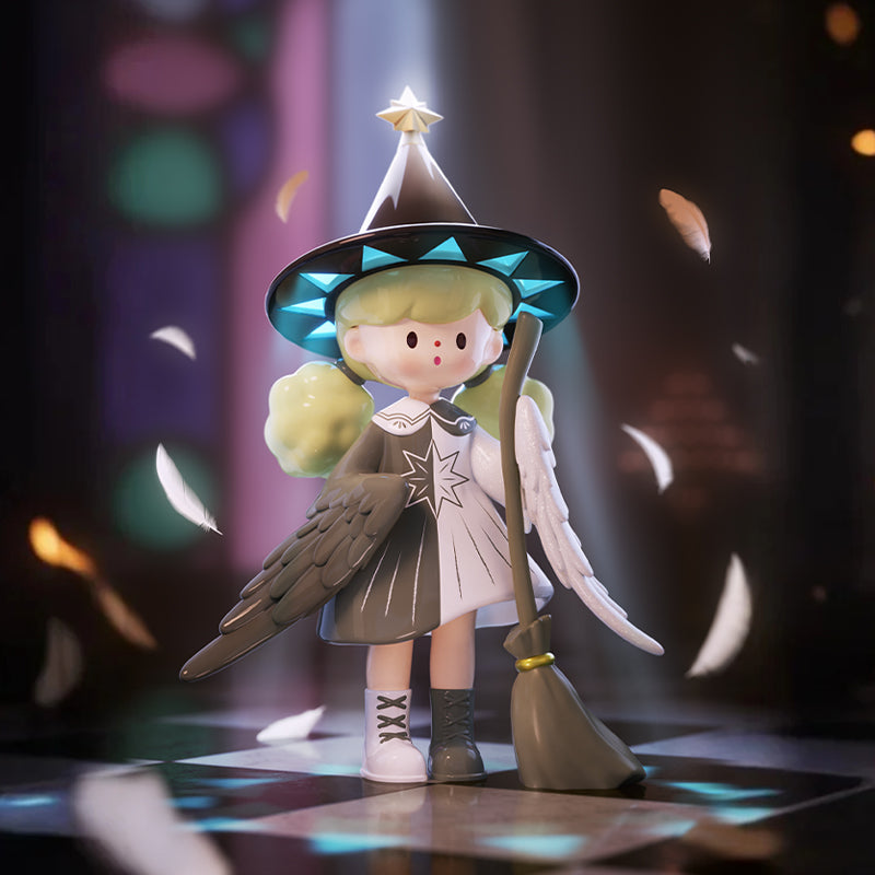 A vinyl figure with light green hair wearing a black pointed hat decorated with blue triangles and a gold star on top. The figure has one black and one white wing, wears a black-and-white dress with a large star design, and holds a gray broom. It stands on a checkered floor with floating white feathers and a blurred background of colored lights.