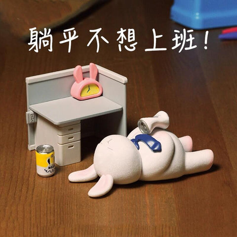 A bunny figurine sprawls flat on the floor in surrender, with beer cans nearby and a desk setup behind it, capturing the mood of giving up on work