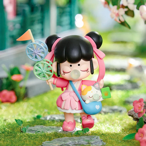 A cheerful collectible figurine from the "Nanci Blooming Girl" series features a girl with black twin buns, dressed in a pink traditional outfit. She carries a blue sling bag with a sleepy cat inside, holding a green flag. In her other hand, she waves colorful spinning pinwheels. Her closed eyes and bubblegum bubble add a playful touch as she walks along a garden path. The lush greenery and blooming flowers create a nostalgic and heartwarming scene reminiscent of childhood joy.