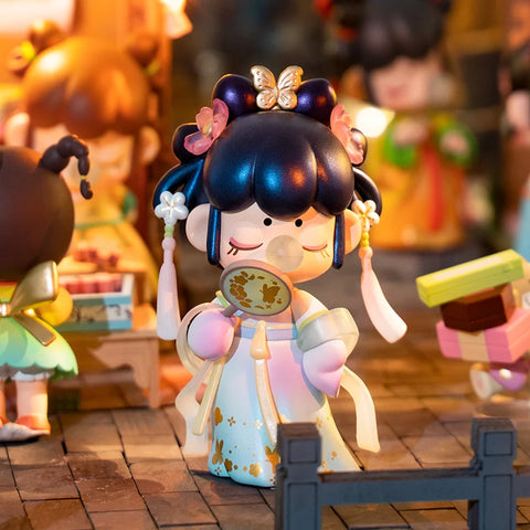 A stunning collectible figurine from the "Nanci Blooming Girl" series features a girl dressed in an elegant pale blue and gold traditional outfit. She holds a delicate hand mirror while blowing a bubblegum bubble, exuding grace and charm. Her intricate hairstyle is adorned with golden butterfly and floral ornaments. Set against a festive night market scene with warm lantern lights and bustling activity, she stands out as a mysterious and enchanting hidden chaser figure.