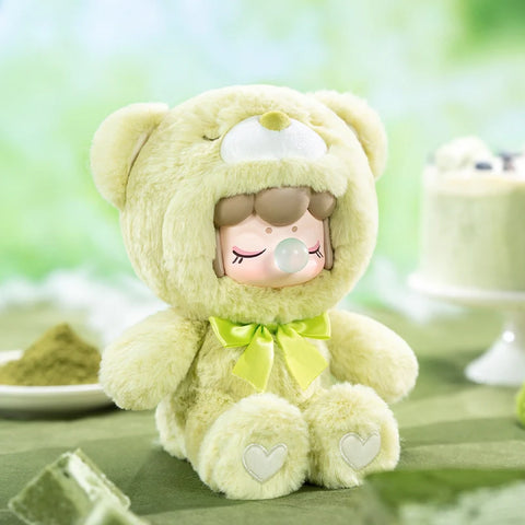 A delightful collectible figurine from the "Nanci Colorful Chocolate Cutie Bears" plush series features a character dressed in a soft, matcha-green bear suit with a matching satin bow. The figure has a serene expression with closed eyes and a bubblegum bubble, while heart-shaped details accent its plush paws. Surrounded by matcha treats and a pastel green backdrop, the cozy and soothing atmosphere perfectly complements the sweet and cuddly aesthetic.