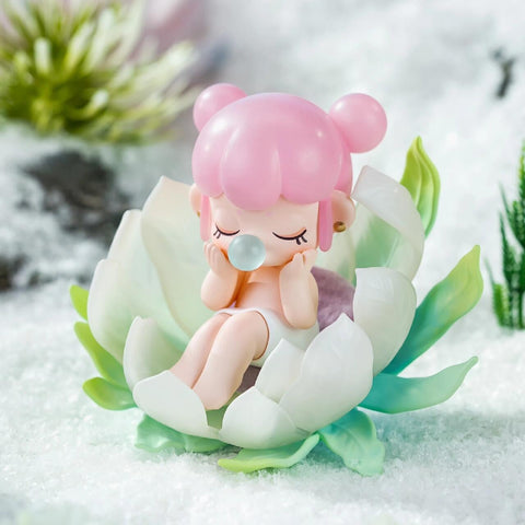 A figurine from the Nanci “Flower Stories” blind box series inspired by the saussurea flower. The character has bubblegum pink hair styled in twin buns and sits curled up peacefully inside a large, soft green and white bloom. With closed eyes and a bubble at her lips, she rests in a snowy landscape that highlights the saussurea’s association with alpine environments and quiet resilience.