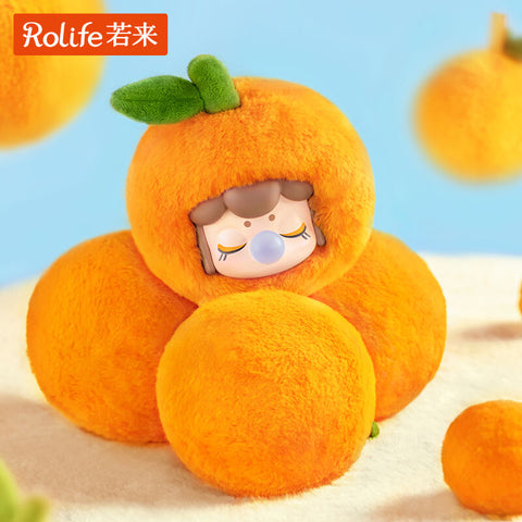 A Nanci Fruit Mood plush designed as a bright orange, round and fuzzy with a green felt leaf sprouting on top. Nestled inside, the figure’s gentle face is seen with closed eyes, bubblegum bubble at its lips, and a peaceful smile, blending cuteness with a citrus fruit theme.