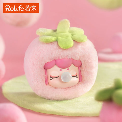A Nanci Fruit Mood plush figure styled as a strawberry, wrapped in fluffy pink fabric with a soft green leafy top. The doll’s serene face has closed eyes with long lashes, a bubblegum bubble at the mouth, and rosy cheeks, capturing a sweet and dreamy fruit-inspired design.
