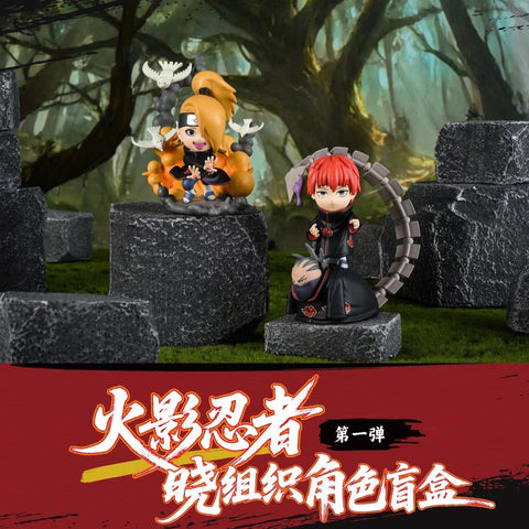 Deidara and Sasori figures are posed on rocky platforms. Deidara is animated with clay birds flying around him, sculpted in orange smoke. Sasori stands in a black cloak with his segmented tail weapon arched behind him, capturing his puppet master style.