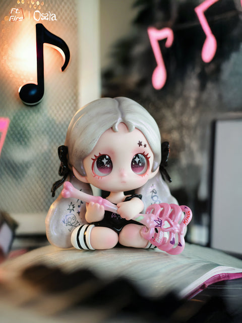 A small figurine with silver-and-black hair sits with a pink skeletal staff and heart-shaped accessories. The figure wears striped socks and a black outfit, framed by neon music notes glowing in the background, representing a “rock” aesthetic.