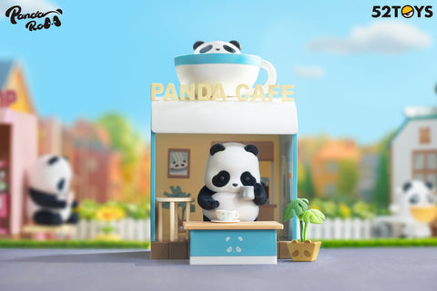 A panda figurine from the 52TOYS Panda Roll Shopping Street series stands inside a small blue-and-white café labeled “Panda Café.” The panda is holding a cup and appears to be sipping a hot drink while standing behind a counter with another cup on it. The café features a large cup with a panda face on the roof, a potted plant, framed artwork, and seating inside. The scene is set against a soft, colorful backdrop with blurred buildings and greenery, creating a cozy and cheerful atmosphere.
