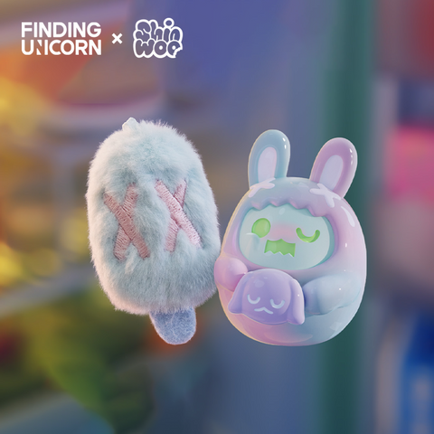 Two small collectible figures float together. The left is a fluffy blue popsicle-shaped plush with stitched pink X marks. The right is a rounded pastel vinyl bunny figure with tall ears, wearing a light blue and lavender hood with white X marks and holding a sleeping bunny plush.